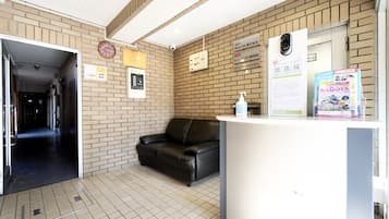 A reception area with a reception desk, a black leather sofa, a clock, and a sign indicating 78 hostel management rooms.