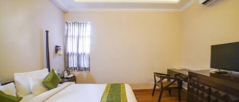 A hotel room with a bed, a desk, a chair, and a television.
