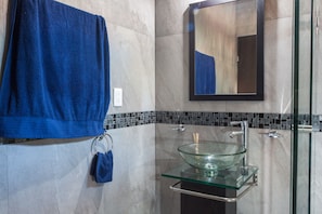 Une salle de bain avec un lavabo en verre, une serviette bleue et un miroir.