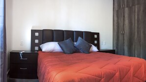 Een slaapkamer met een bed, nachtkastjes, een kledingkast en een deur.