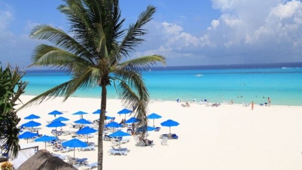 Een strand met wit zand, helderblauw water en palmbomen.