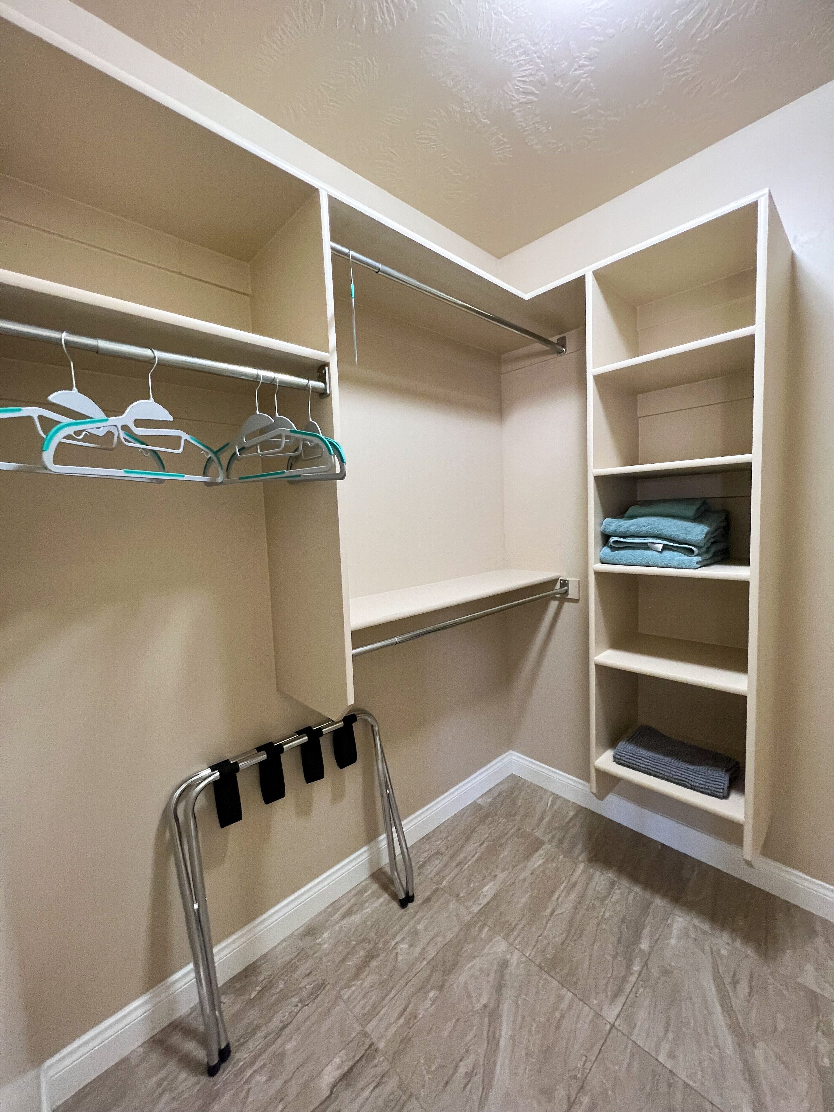 A walk-in closet with open shelves, a metal rack with hangers, and a step stool.