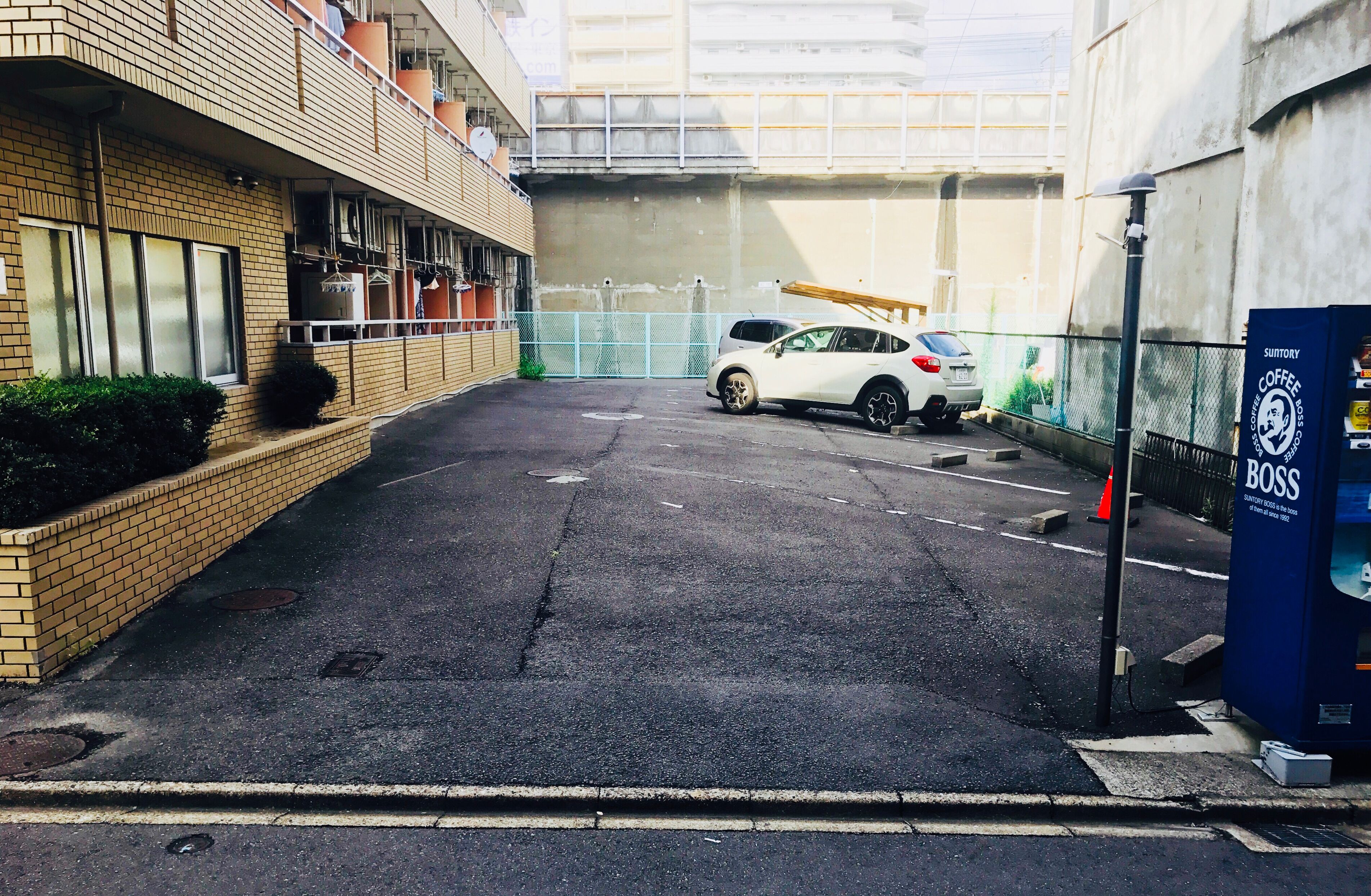 A parking area with a white car and a blue vending machine labeled 'Sutory Coffee Boss'.