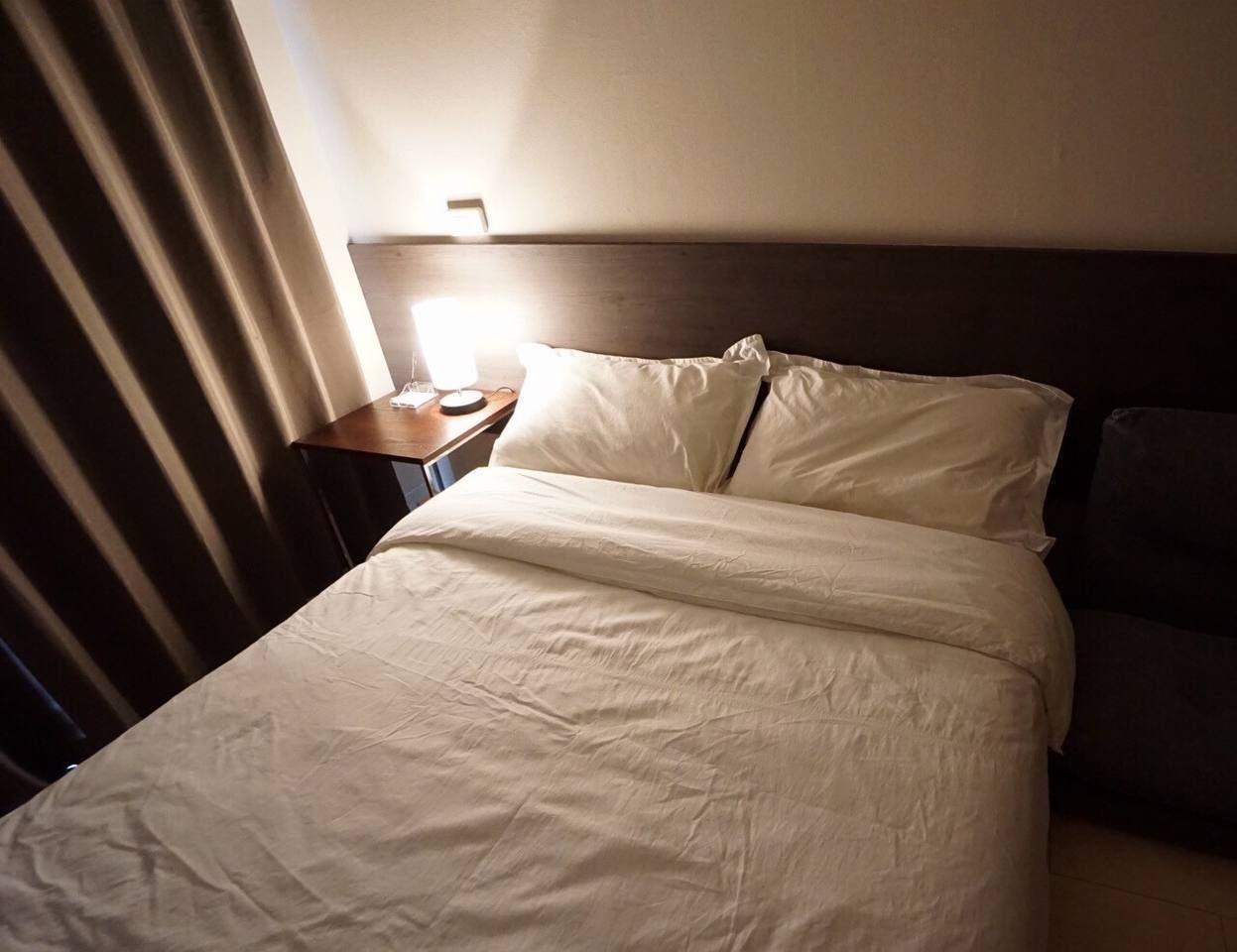 A hotel room with a bed, a nightstand, and a lamp.