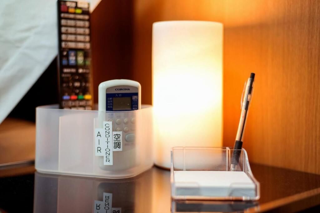 A hotel room with a bedside table featuring a Corona phone, a candle, and a pen holder.