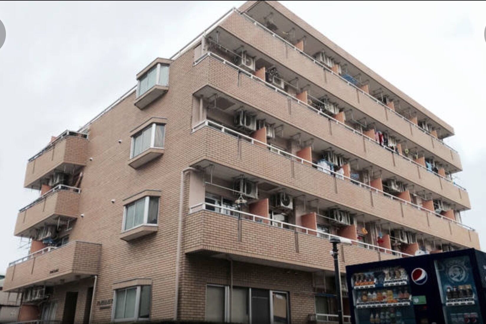 A multi-story brick building with balconies, air conditioning units, and a vending machine.