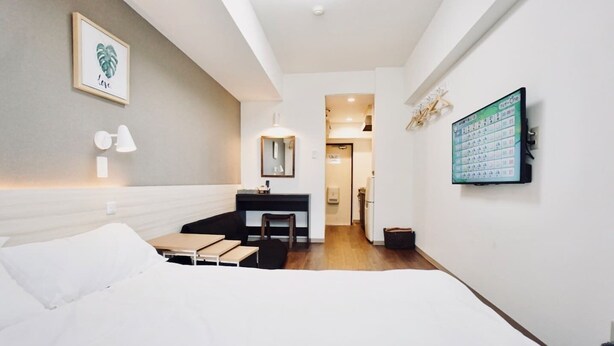 Une chambre d’hôtel moderne équipée d’un lit, d’un bureau et d’une chaise, d’une petite kitchenette et d’un calendrier accroché au mur.
