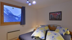 Ein Schlafzimmer mit Bett, Fenster mit Bergblick, Heizkörper und einem gerahmten Bild an der Wand.