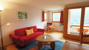 Ein gemütliches Wohnzimmer mit einem roten Sofa, einem Holztisch und Blick auf einen Wald durch große Fenster.