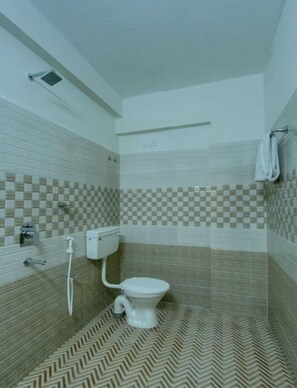 A bathroom with a toilet, a shower, and a towel rack. - Sweven Stays (Mangaluru)