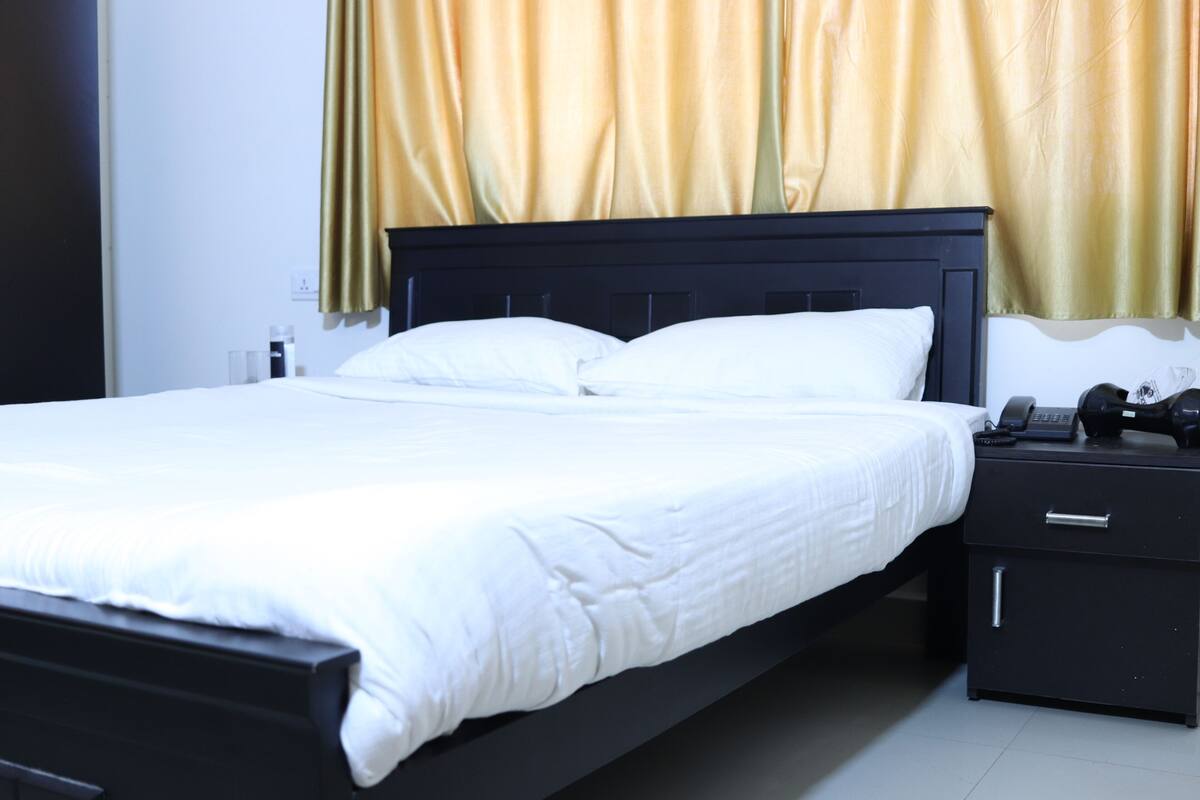 Una cama bien hecha con sábanas blancas, cabecera negra y mesita de noche con lámpara y teléfono.