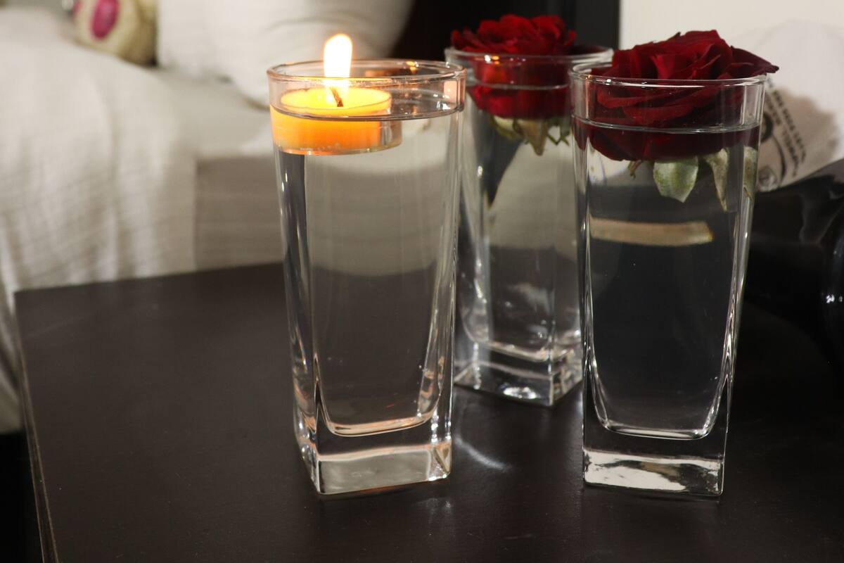 Tres jarrones de vidrio transparente con agua y rosas sobre una mesa oscura.