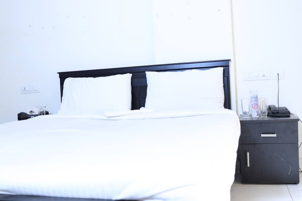 Una habitación de hotel con una cama, una mesita de noche, un teléfono y un armario pequeño.