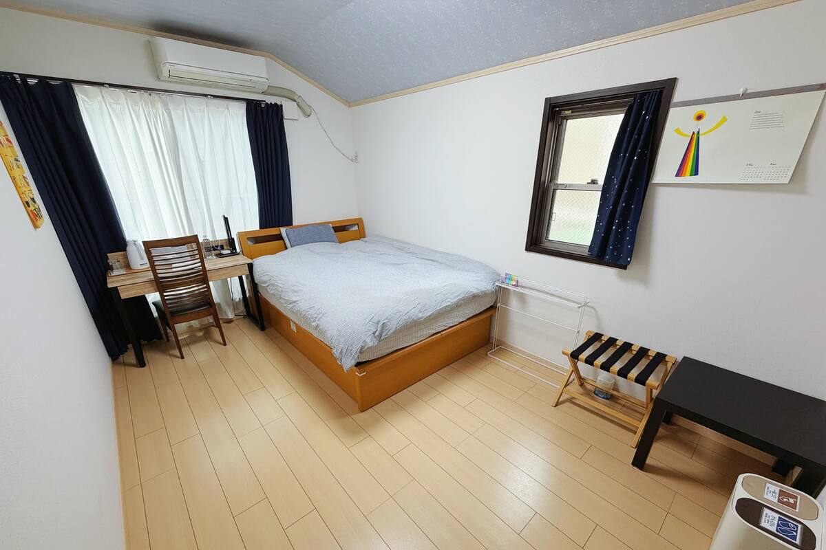 Una camera da letto con un letto, una scrivania, una sedia, condizionatore d'aria, finestra con tende e un calendario appeso al muro.