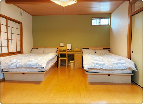 A room with two beds, a desk, a chair, a window, and a traditional sliding door. - Hao Bros. Home WA (Tokyo)