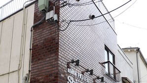 A hotel with a brick facade, a large garage door, and visible electrical equipment. - Mini Hotel Shinjuku Front 101 (Tokyo)