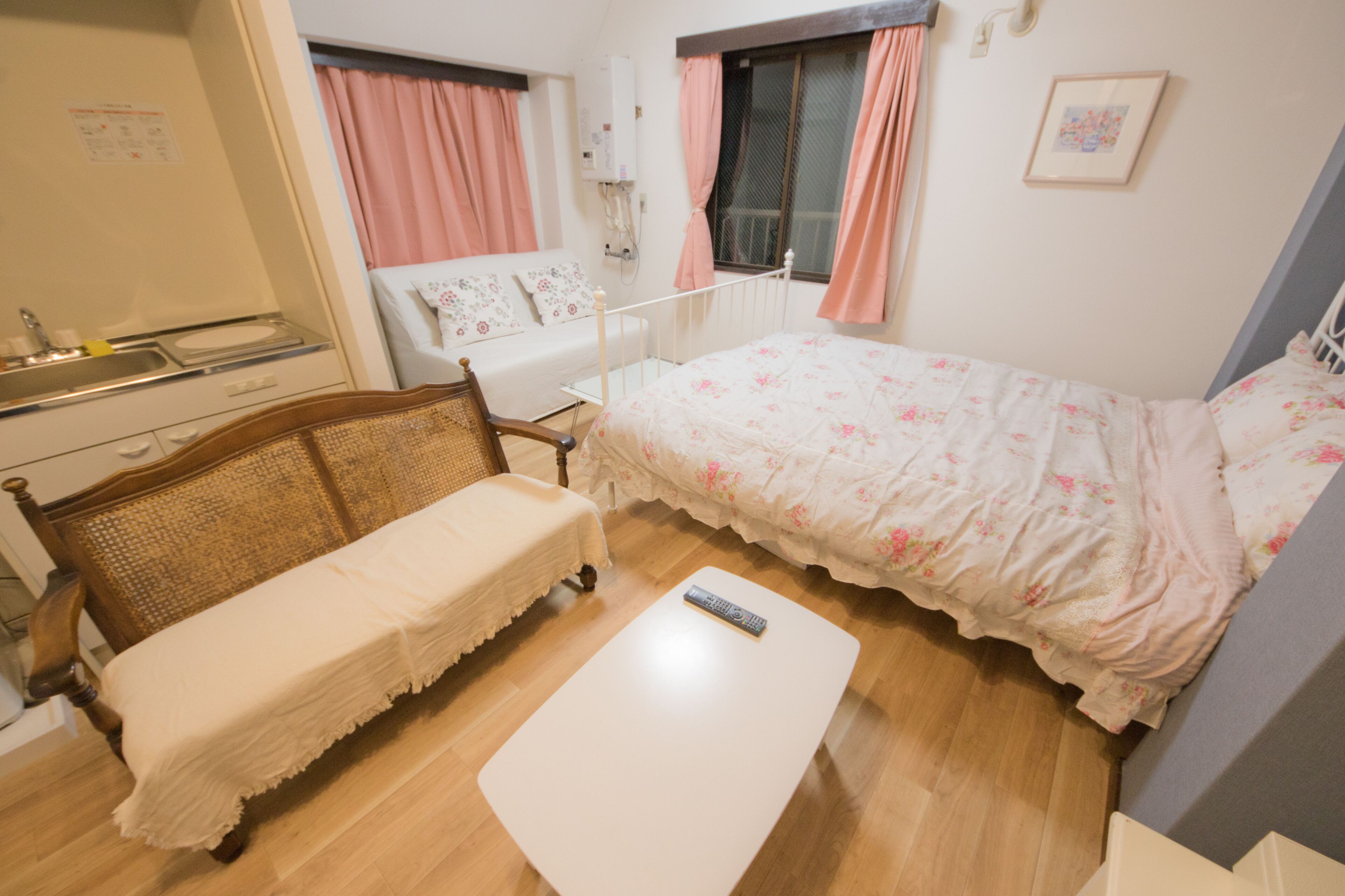 A bedroom with a bed, a bedside table, a small sofa, a window with curtains, a wall-mounted light, and a picture on the wall.