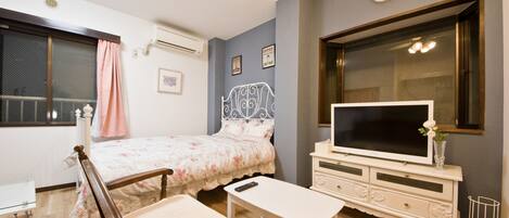 Un dormitorio con cama, mesita de noche, televisión, cómoda y ventana con cortinas.
