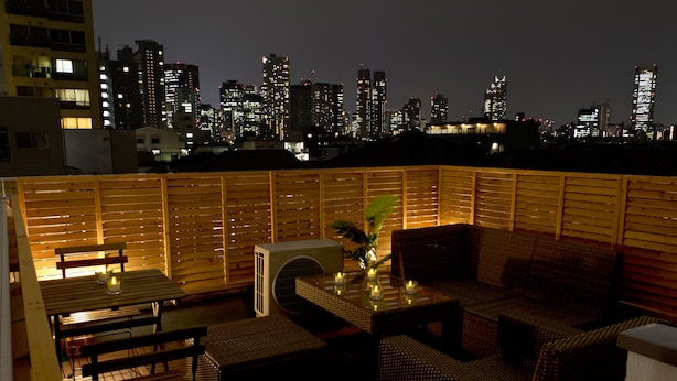 A rooftop terrace with a city skyline view, furnished with wicker furniture and a table with candles. - Mini Hotel Shinjuku Front 101 (Tokyo)