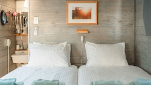 Un letto matrimoniale con biancheria da letto bianca e asciugamani azzurri, una parete in legno, un quadro incorniciato e un comodino con una lampada.