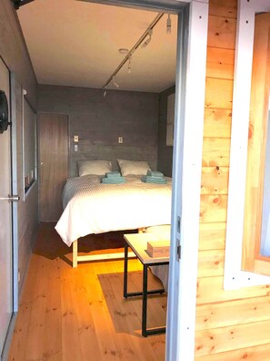 Cozy retreat with a bed, table, and bench, set against a sloped ceiling with a light fixture.