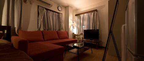 A living room with a red sofa, a glass coffee table, a television, and a refrigerator.