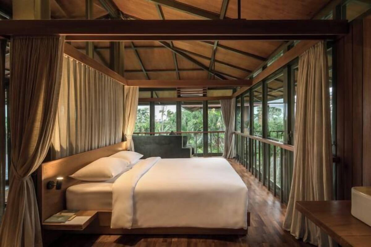 Ein geräumiges Schlafzimmer mit einem großen Bett, Holzbalken und Blick ins Grüne durch große Fenster.