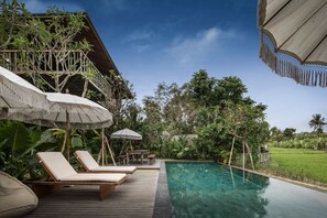 Ein Poolbereich mit Liegestühlen und Sonnenschirmen, umgeben von üppiger Bepflanzung und einer Holzterrasse.