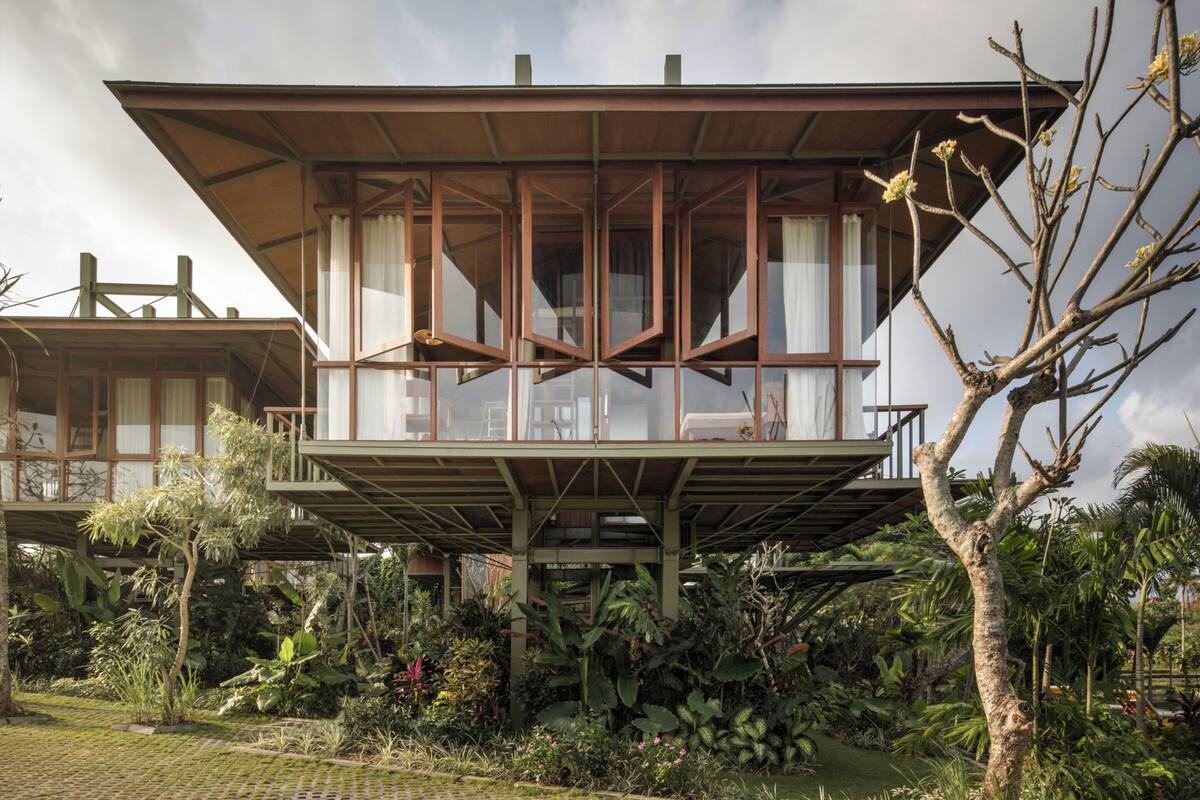 Ein zweistöckiges Holzhaus mit großen Fenstern und einem Balkon, umgeben von üppiger tropischer Vegetation.
