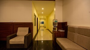 A hotel lobby with a long corridor, two armchairs, a water dispenser, and a reception desk. - Woodside Residency Thekkady (Peermade)
