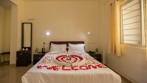 A neatly made bed with a heart-shaped flower arrangement and the word "welcome" spelled out in petals. - Woodside Residency Thekkady (Peermade)