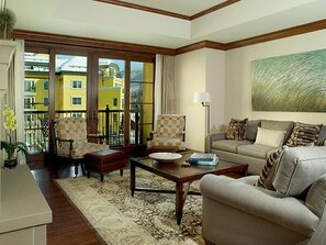 A living room with a sofa, armchairs, a coffee table, and a view through a glass door to a yellow building.