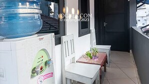 A narrow corridor with a water dispenser, a white chair, and a small table. - Penginapan Pugeran - Hostel (Yogyakarta)