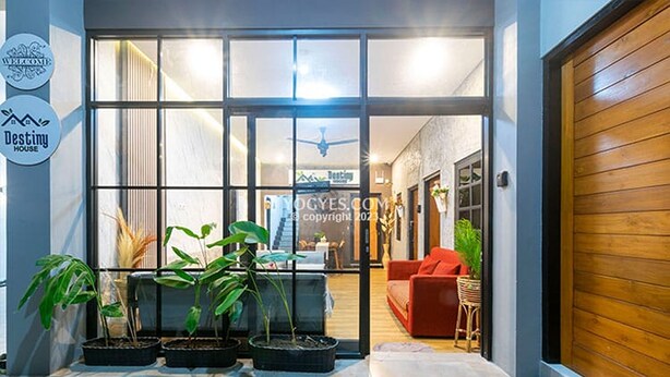 A modern entrance with a glass door, potted plants, and a red sofa inside. - Penginapan Pugeran - Hostel (Yogyakarta)