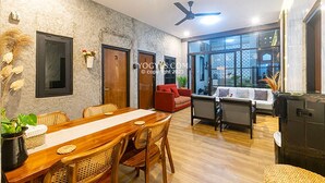 A spacious living area with a wooden dining table, wicker chairs, a red sofa, and a large window offering a view. - Penginapan Pugeran - Hostel (Yogyakarta)