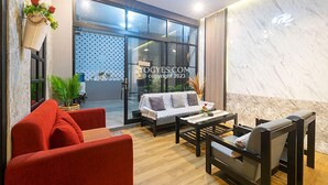 A modern living room with a red sofa, a grey sofa, and a coffee table. There is a large window with a view of the outside. - Penginapan Pugeran - Hostel (Yogyakarta)