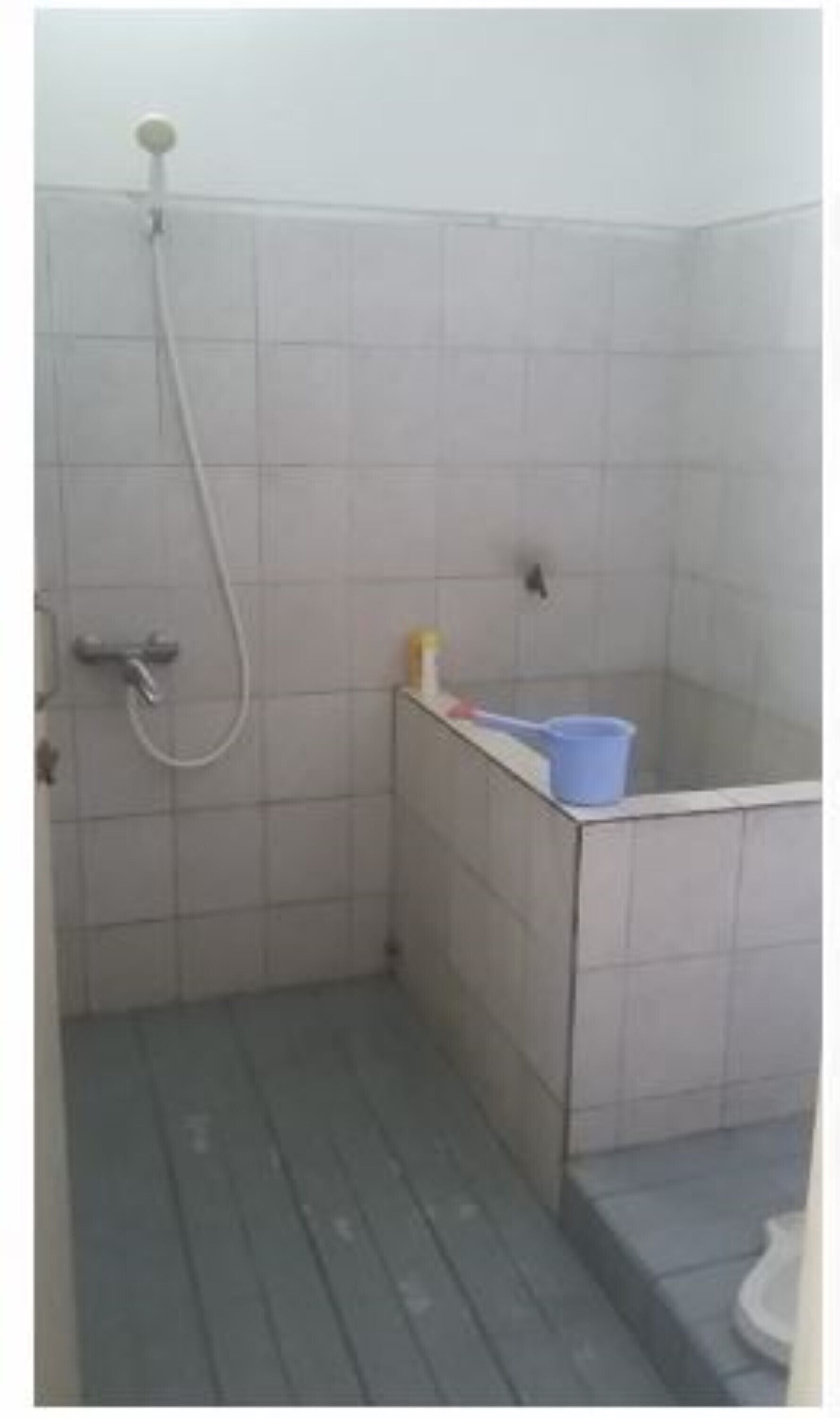 A small, tiled shower area with a handheld showerhead and a blue bucket.
