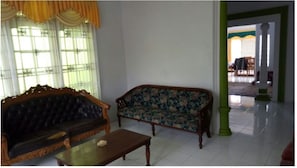 A room with a dark-colored sofa, a wooden coffee table, and a patterned armchair. - Villa Darsono (Batu)