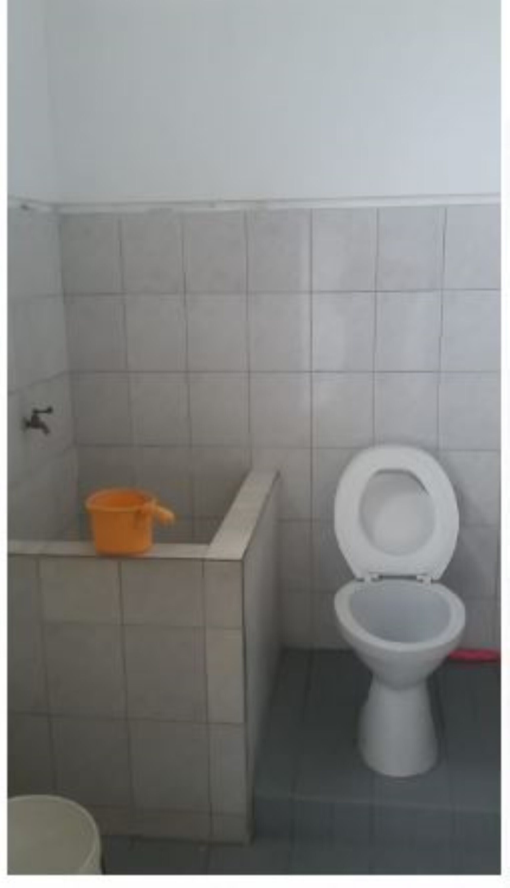 A bathroom with a toilet, a small orange bucket, and a white toilet paper holder.