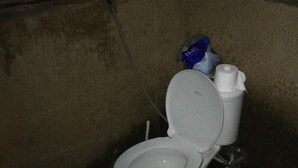 A toilet in a dimly lit, confined space with a visible pipe and a bag of tissues on the tank. - Tegal Dukuh Camp (Taro)