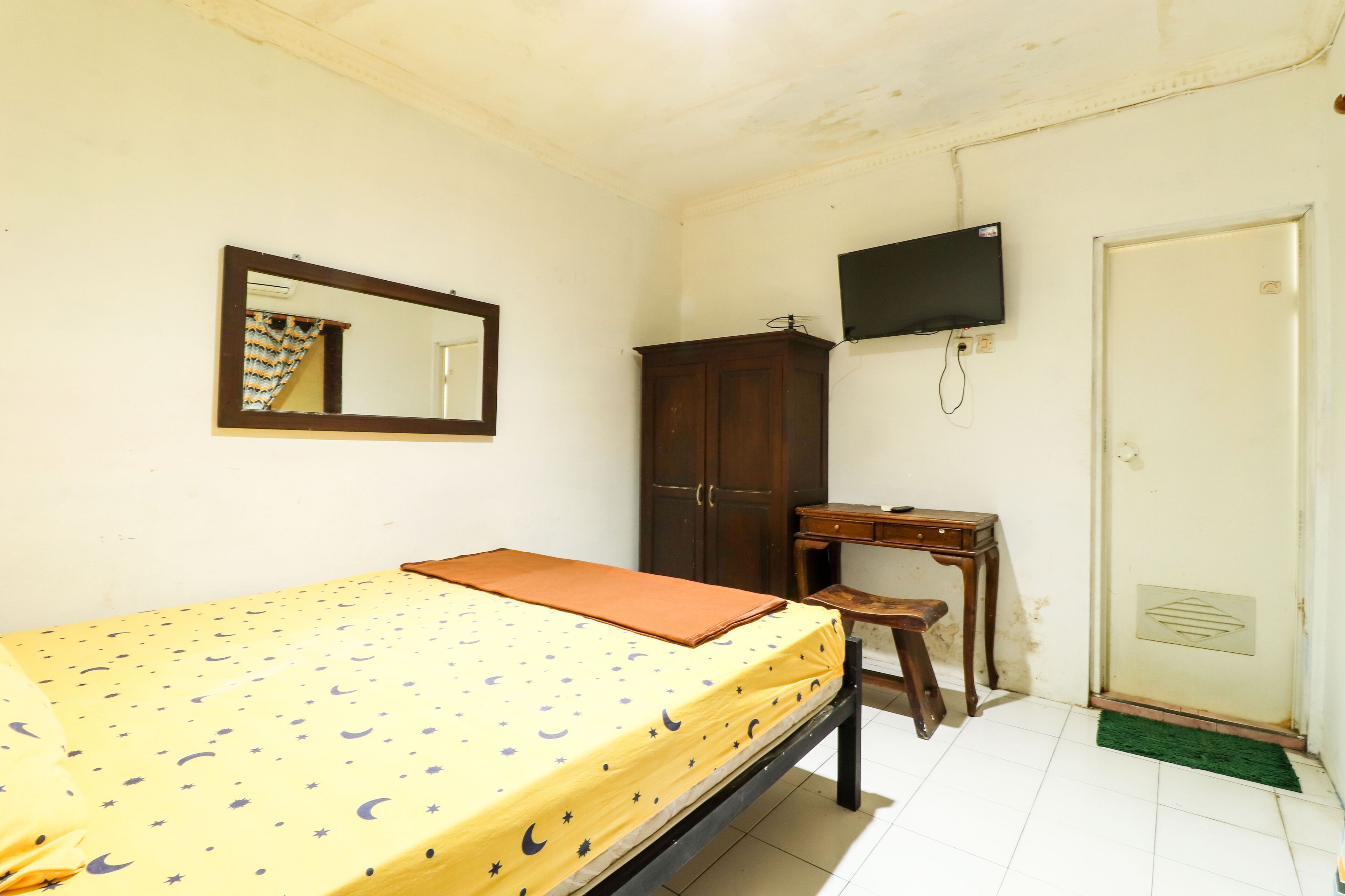 Una habitación pequeña y sencilla con cama, escritorio, espejo y televisor.