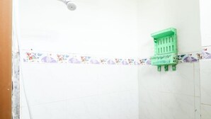 A bathroom with white tiled walls, a showerhead, a toilet, and a green shelf. - Kos VIP Josh (Pogung Lor)