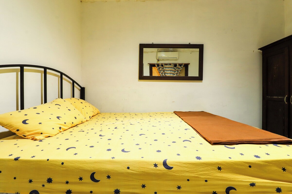 A bed with a yellow bedspread featuring a star and crescent pattern, a brown blanket, and a black metal headboard.
