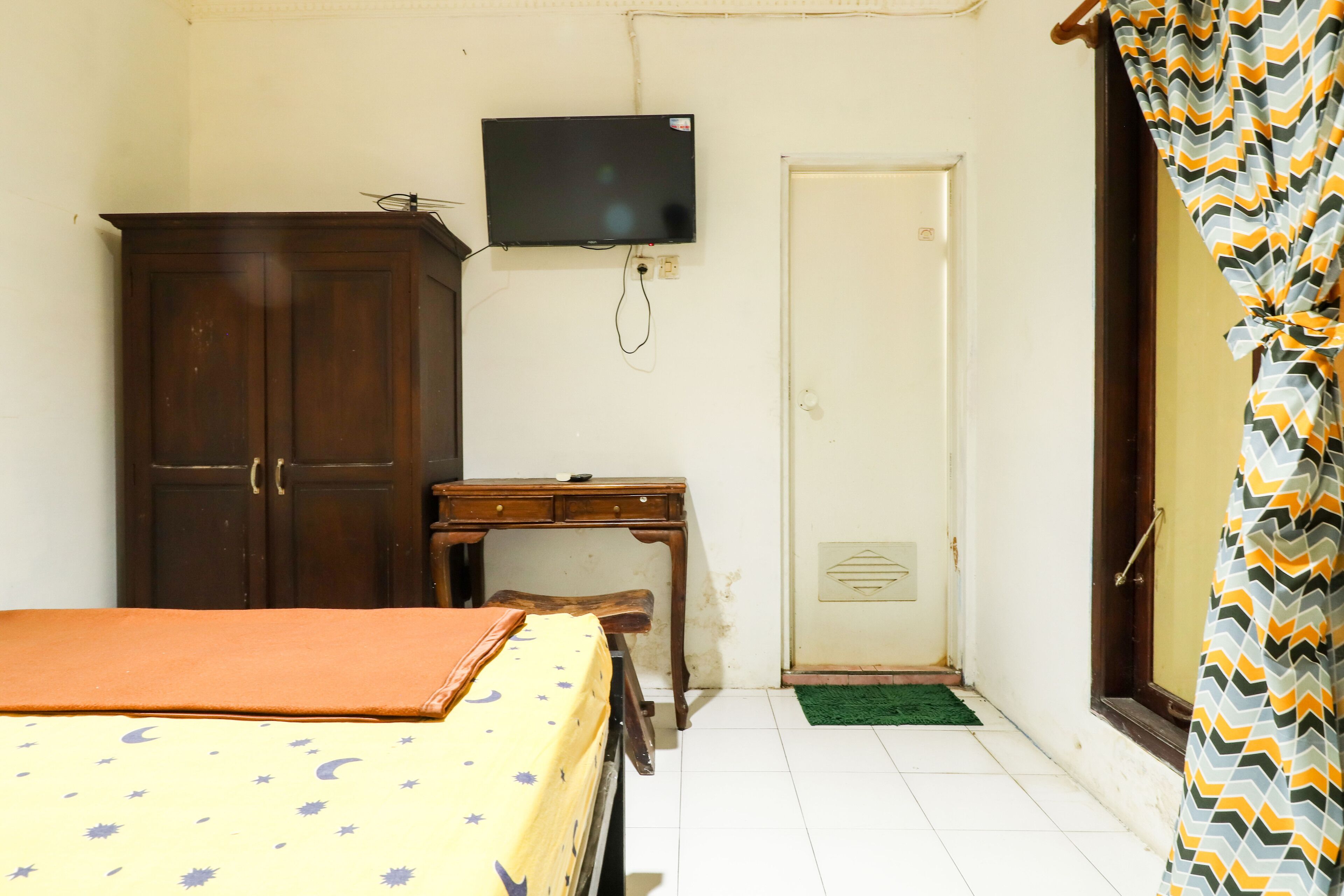 Une chambre à coucher comprenant un lit, un bureau, une armoire, un téléviseur et une porte.
