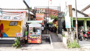 A street scene with a food cart labeled "Rachel Juice" and a building with a sign that reads "KOST VIP JOSH ROOM AVAILABLE". - Kos VIP Josh (Pogung Lor)