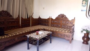 A traditional wooden sofa with intricate carvings, a glass coffee table, and a potted plant. - Cheap Inn - Hostel (Banyuwangi)