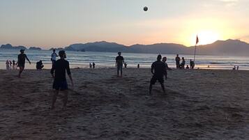A beach scene with people playing volleyball, a flag, and distant mountains.