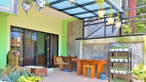 A cozy patio area with a wooden bench, a table, and a variety of potted plants. - Cheap Inn - Hostel (Banyuwangi)