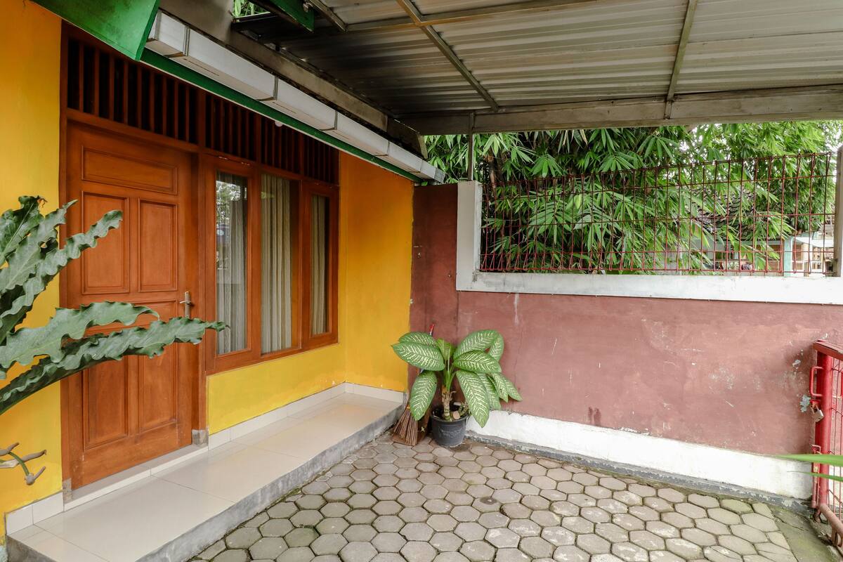 A house with a tiled patio, a wooden door, a potted plant, and a metal fence.