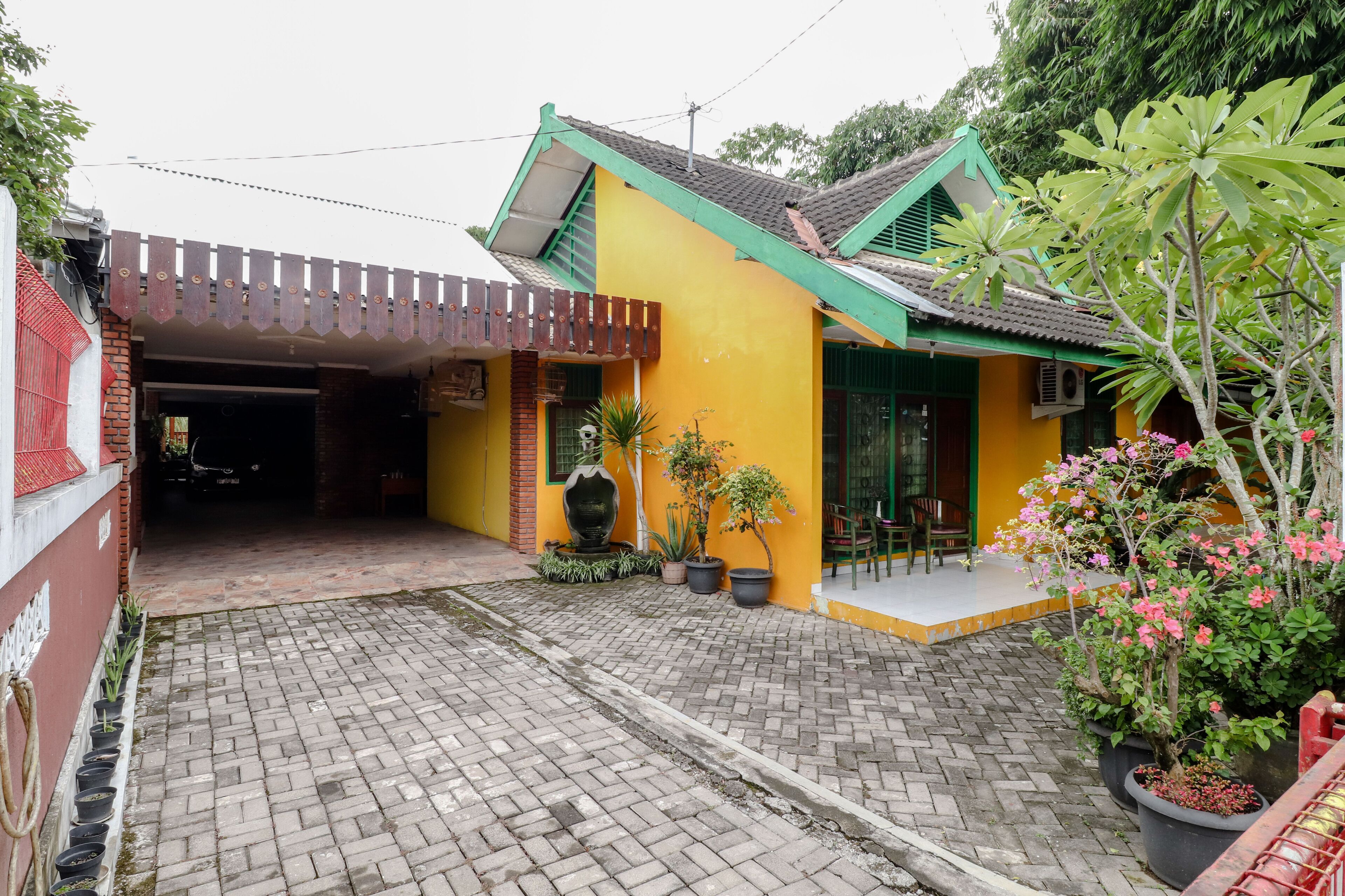 A yellow building with a green roof, a paved entrance, and potted plants.